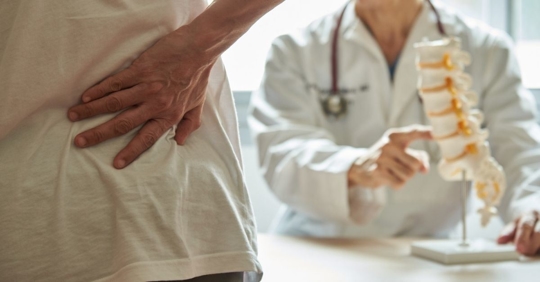 Patient with hand on his back in front of a doctor with a model of a spinal cord
